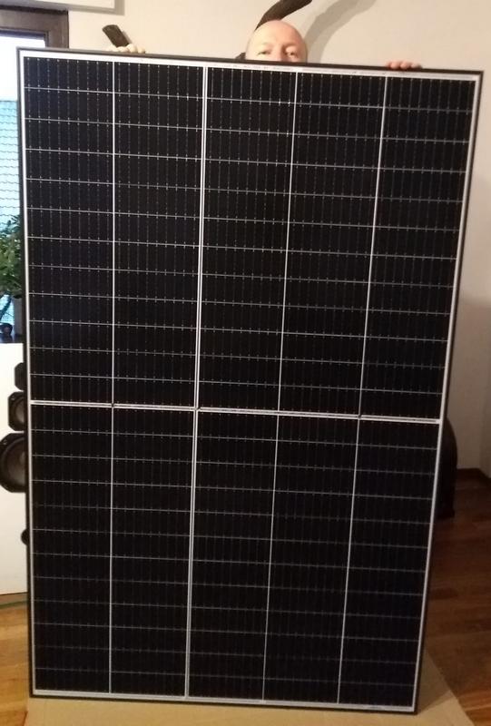 Ein Solarpanel, welches Hochkant auf dem Boden steht. Dahinter lugt ein Mann hervor, der gerade so über das Panel schauen kann.