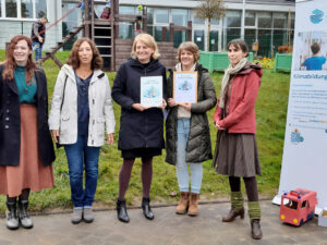 Fünf Frauen stehen vor der Kita Siegpiraten, zwei halten freudestrahlend jeweils eine Urkunde in die Kamera.