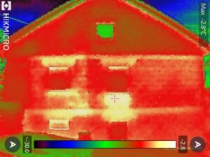 Das Wärmebild einer Hauswand mit Giebel. Deutlich zu sehen sind Wärmebrücken ober und unterhalb der Fenster.
